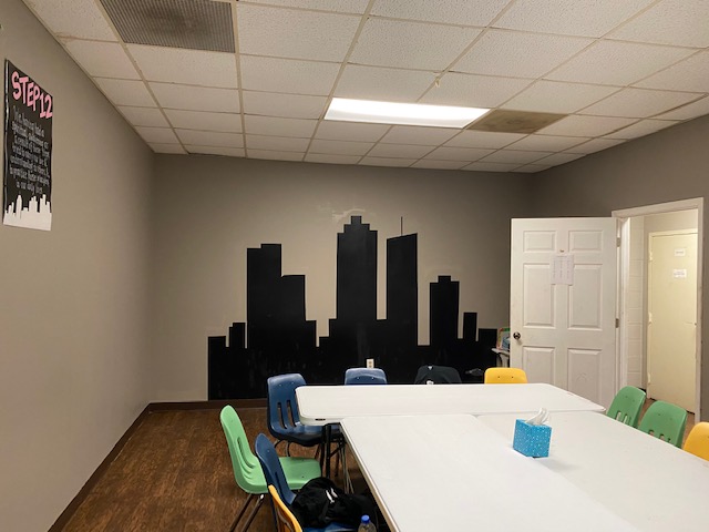 room with tables and chairs with a mural of the city on the wall