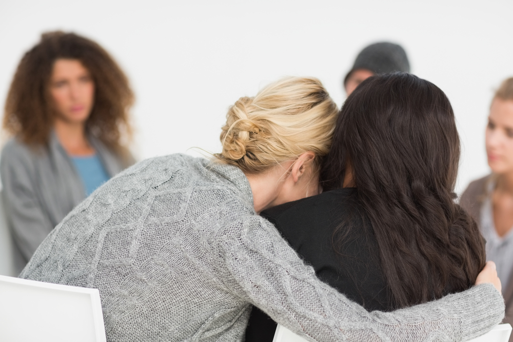 women sitting in a circle and 2 women hugging.