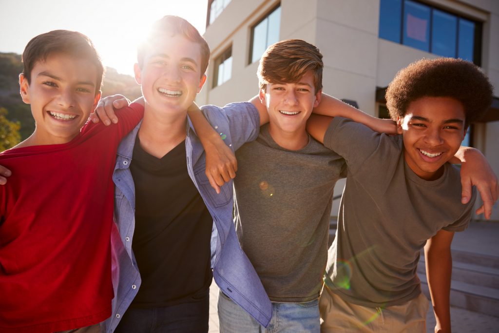 4 teenage boys with their arms around each others shoulders, smiling.