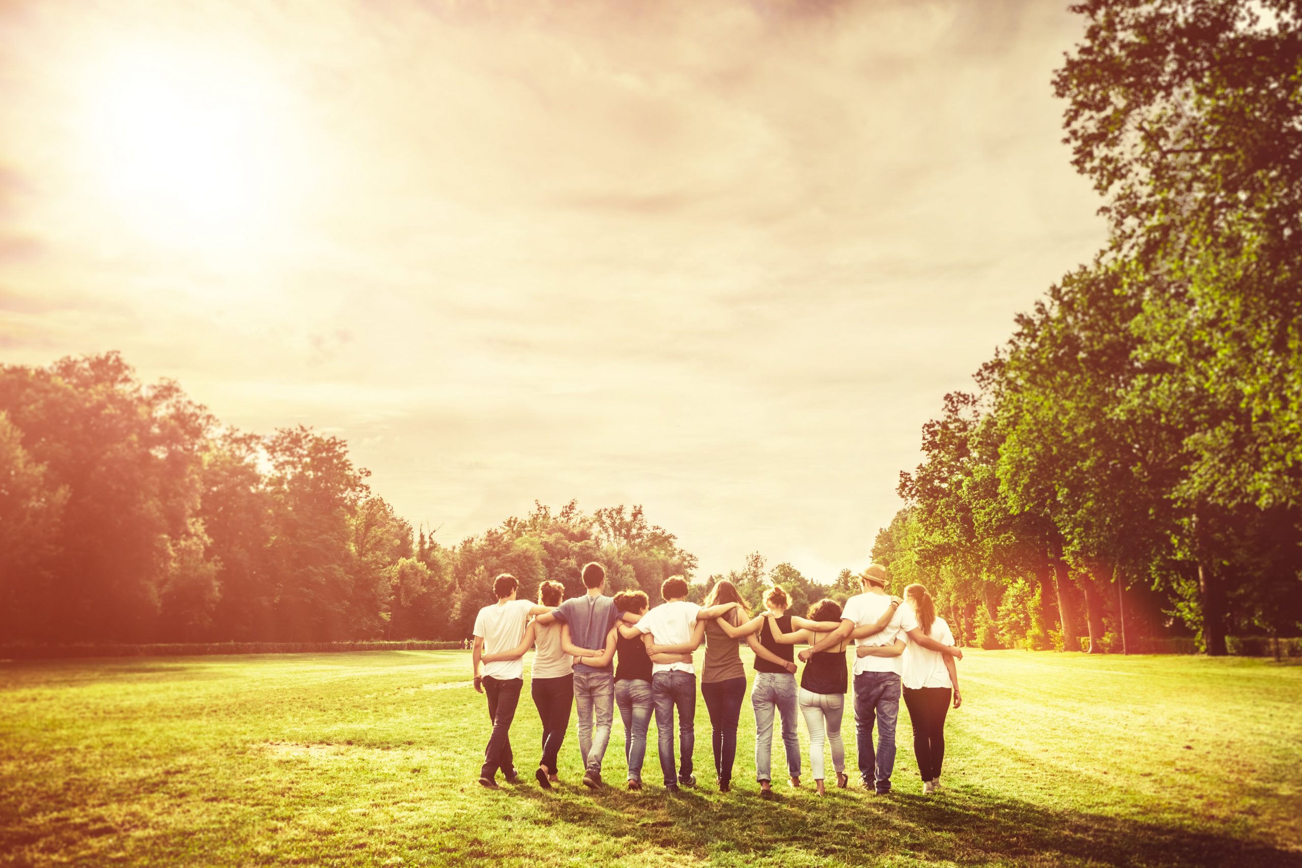 young adults side-by-side holding each others shoulders in a field with trees in the background.