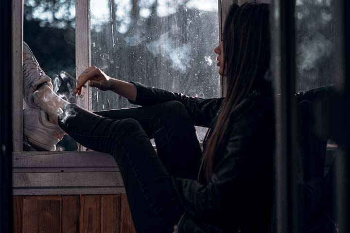 teen smoking with legs hanging out the window